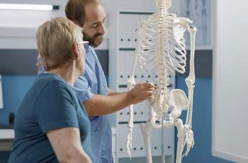Un ostéopathe montre à sa patiente un endroit de la colonne vertébrale sur modèle anatomique de squelette humain.